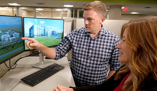 At Fluor office, man and woman meet and he points to a photo of a project on a computer screen